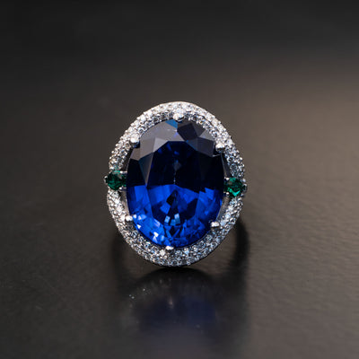 טבעת ייחודית עם שיבוץ אבן חן ספיר כחולה אובלית גדולה במיוחד עם אבני חן אמרלד ירוקים בצדדים ויהלומים מסביב