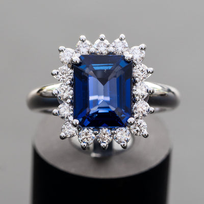 טבעת אירוסין משובצת אבן חן ספיר כחולה בחיתוך אמרלד מסביב יהלומים קטנים למראה יוקרתי