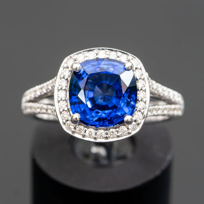 טבעת אירוסין מקורית משובצת אבן חן ספיר כחולה בחיתוך קושן בצדדים ומסביב לאבן יהלומים קטנים